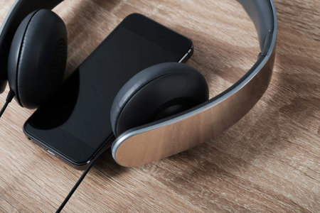 Blank screen mobile phone connecting with headphone on wooden table