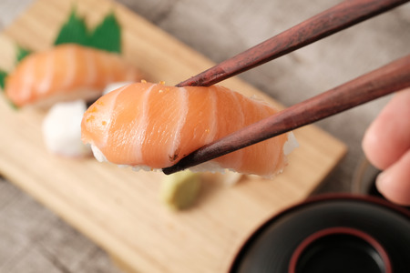 Chopsticks holding  fresh japanese salmon sushi, octopus sushi, ginger, wasabi,soy source and soup in backgroundの写真素材