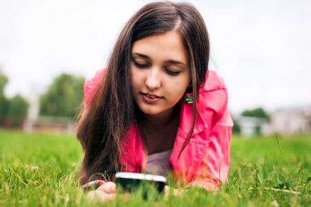 Beautiful girl in the summer in the park, lying on the grass and write SMS, use the Internet on your phoneの写真素材