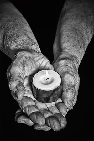 View of the old woman hands holding a burning candle on a black backgroundの写真素材