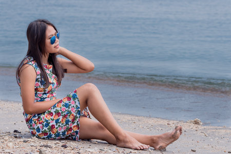 Young attractive indonesian girl sitting on a sandy beach with a sea backgroundの写真素材