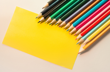 Colored Pencils isolated on white backdrop and blank Yellow note, placed in arc rowの写真素材