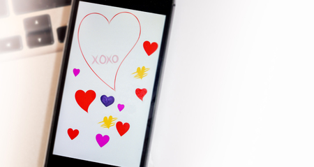 Mobile phone placed on laptop showing Valentine greeting, colored heartsの写真素材