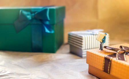 Miniature mailmen figurine carrying package while standing on present box, copy spaceの写真素材