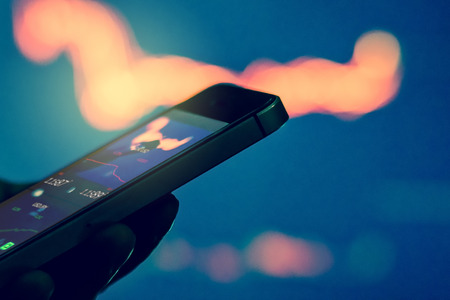 Trader in dark using mobile phone against stock market chartsの写真素材