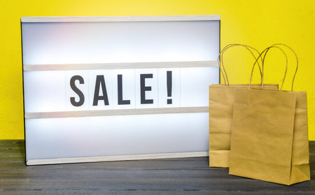 Light box with Sale letters and small shopping bags against yellow background