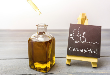 Cbd oil in glass bottle and chalkboard with molecule drawing on wooden tableの写真素材