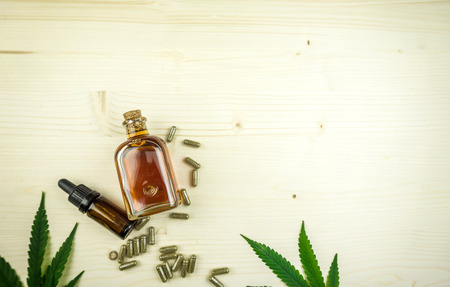 Clear CBD Cannabidiol capsules and cannabis oil on wooden backdrop,flat layの写真素材