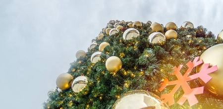 Looking up a big Christmas tree against cloudy sky outdoors