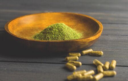 Mitragynina speciosa or Kratom powder in wooden bowl and Kratom capsules on tableの写真素材