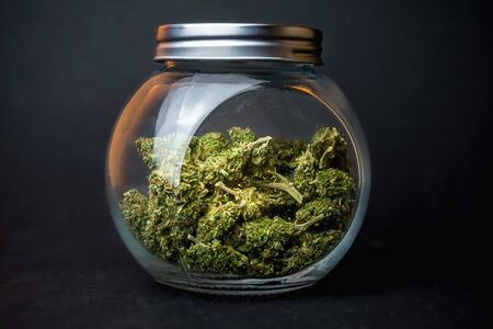 Medical Marijuana flower buds in glass jar on dark backdropの写真素材