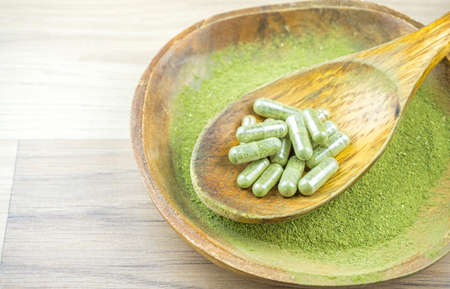 Kratom Mitragyna Speciosa an alternative medicine powder and capsules in wooden spoon bowlの写真素材