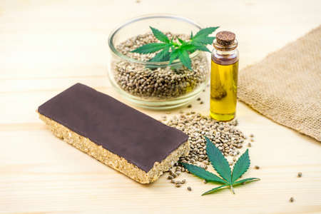 Cannabis seeds in bowl oil and hemp seed cereal bar with chocolate on tableの写真素材