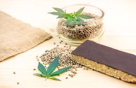 Cannabis seeds in bowl and hemp seed cereal bar with chocolate on tableの写真素材