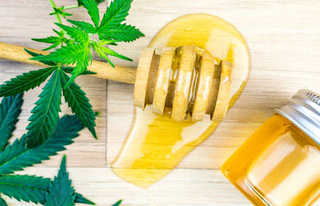 CBD Cannabis infused Honey with dipper spoon jar Marijuana leafs on wooden table, Cannabis products in food industryの写真素材