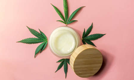 CBD Cannabidiol Hand skin care moisturizer and Cannabis leafs on pink backgroundの写真素材