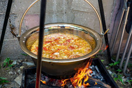 Pot with vegetables cauldron over open fire, preparing stew soup on wood grill, outdoor cookingの写真素材