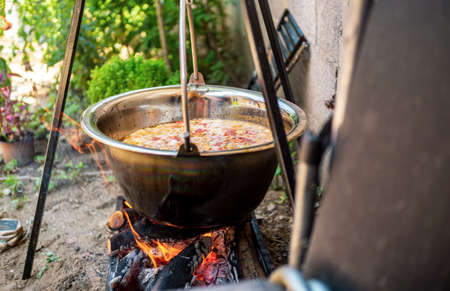 Pot with vegetables cauldron over open fire, preparing stew soup on wood grill, outdoor cookingの写真素材