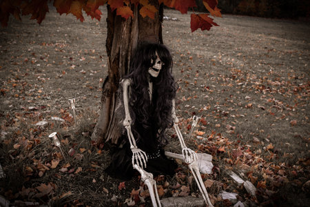 This female skeleton with dark hair is sitting under a tree during autumnの写真素材