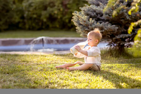A little boy is sitting on the Bank of the river. Looks at the water. Swinging his legs in the water. Enjoys a walk in nature.の写真素材