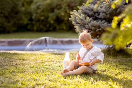 A little boy is sitting on the Bank of the river. Looks at the water. Swinging his legs in the water. Enjoys a walk in nature.の写真素材