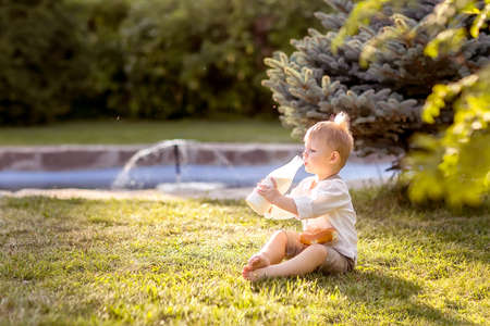 A little boy is sitting on the Bank of the river. Looks at the water. Swinging his legs in the water. Enjoys a walk in nature.の写真素材