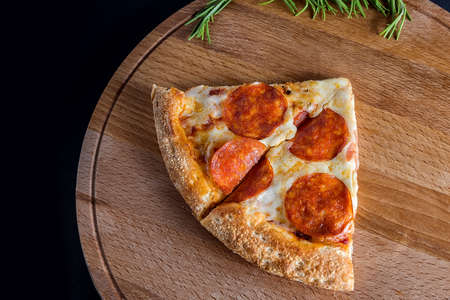 A slice of pepperoni Pizza sits on a wooden cutting Board against a dark background.Four different pizza flavors. Space for text. The view from the top.の写真素材