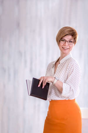 Portrait of a happy woman standing with a Notepad and pen. A business woman thinks through and writes her work plan. Successful small business owner in business attire.の写真素材
