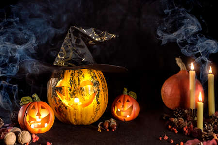 Carved Pumpkins for Halloween, Jack's head is on the table. Pumpkin in a witch's hat. Smoking a lighted candle. Dark background.の写真素材