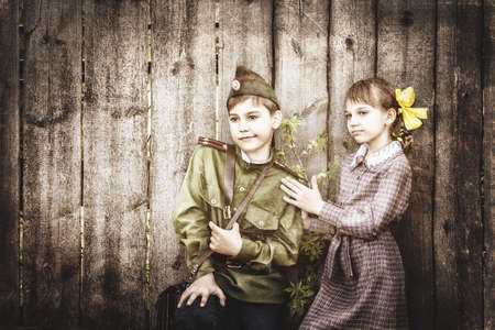 Postcard, stylized as vintage for the Victory Day. A boy in a military uniform and a girl in an old dress. The theme of May 9, Victory Day in Russia. Soft selective focus, added noise.の写真素材