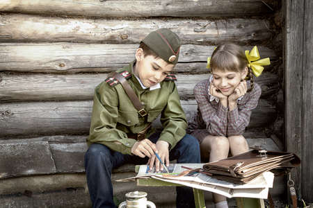 Postcard, stylized as vintage for the Victory Day. A boy in a military uniform and a girl in an old dress. The theme of May 9, Victory Day in Russia. Soft selective focus, added noise.の写真素材