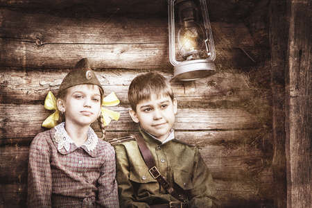 Postcard, stylized as vintage for the Victory Day. A boy in a military uniform and a girl in an old dress. The theme of May 9, Victory Day in Russia. Soft selective focus, added noise.の写真素材