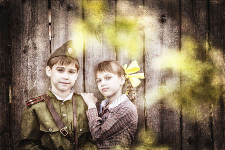 Postcard, stylized as vintage for the Victory Day. A boy in a military uniform and a girl in an old dress. The theme of May 9, Victory Day in Russia. Soft selective focus, added noise.の写真素材