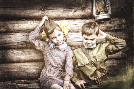 Postcard, stylized as vintage for the Victory Day. A boy in a military uniform and a girl in an old dress. The theme of May 9, Victory Day in Russia. Soft selective focus, added noise.の写真素材