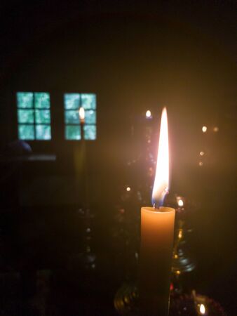 A yellow candle with a long flame in the altar of an Orthodox church near the throne with a menorah opposite the window in the twilightの写真素材