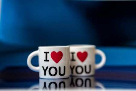 Two white cups with a red heart and the inscription I love you on a classic blue backgroundの写真素材