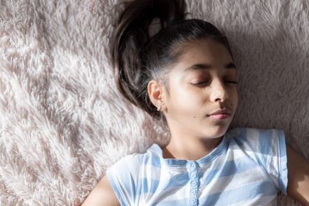 Middle Eastern young cute girl lies on a light beige bed with her eyes closed in the sunlight. Persian swarthy girl on the bed. Middle Eastern children on the bed.の写真素材
