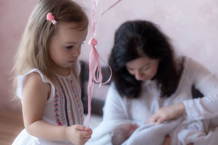 A little girl stands on the bed holding balloons by the ribbon against the background of a grandmother with a little granddaughter in her arms.の写真素材