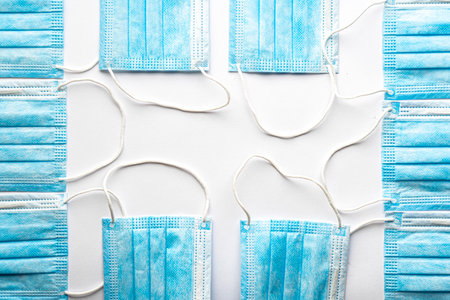 Several medical blue disposable face shields on top of another on a white background copy space. A surgical dressing closes the mouth and nose. Healthcare, medicine, covid-19, epidemic concept.の写真素材