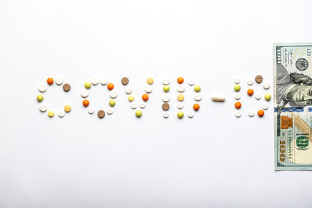 covid-19 inscription with pills and capsules and 100 dollar bill in layout on a white background...