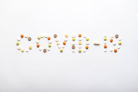 covid-19 inscription with pills and capsules flat lay on a white background copy space. Coronavirus, medicine and health, safety concept.の写真素材