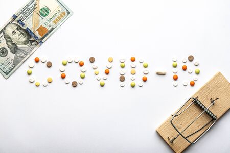 covid-19 inscription with pills and capsules with hundred dollar bill and old wooden mousetrap in flatly on a white background copy space. Coronavirus, medicine and health, safety concept.の写真素材