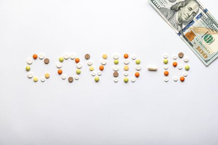 covid-19 inscription with pills and capsules and 100 dollar bill in layout on a white background copy space. Coronavirus, medicine and health, safety concept.の写真素材