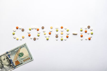 covid-19 inscription with pills and capsules and 100 dollar bill in layout on a white background copy space. Coronavirus, medicine and health, safety concept.の写真素材