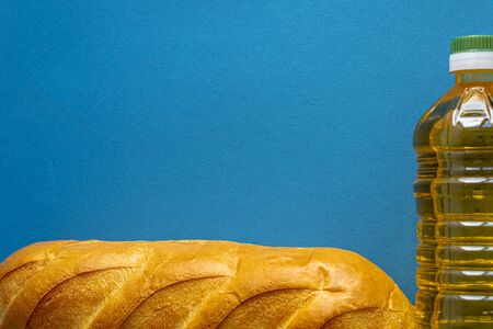Donation, alms, healthy nutrition, humanitarian aid, pandemic, Covid-19 concept. Flatly composition of vegetarian food bottles of sunflower oil and loaf on a blue background, copy spase.の写真素材