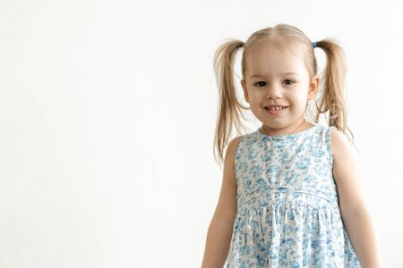 childhood, emotions concept - medium plan isolate little cute three year old girl with two ponytails in a blue dress cute smiles on a white background copy space.の写真素材