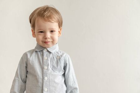 childhood, emotions concept - medium plan isolate little cute two-year-old blond-haired boy in a gray shirt shows grimaces on a white background copy space.の写真素材