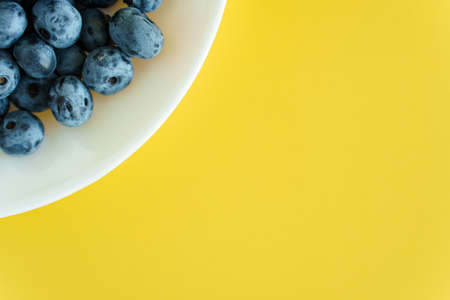 fruit and oat, vitamin, healthy food and drink, traditional medicine, gastronomy concept - layout of purple and blue blueberry berries in white plate or vessel on bright yellow background copy spaceの写真素材