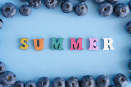 Healthy food, diet, gastronomy, fruits and berries, Harvesting, marketing, fitness concept - layout banner frame closeup of blueberries with inscription summer on plain blue background copy spaceの写真素材