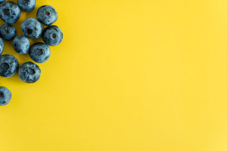 Healthy food, diet, gastronomy, fruits and berries, Harvesting, marketing, fitness concept - layout banner closeup of handful of fresh blueberries scattered on plain yellow background copy spaceの写真素材